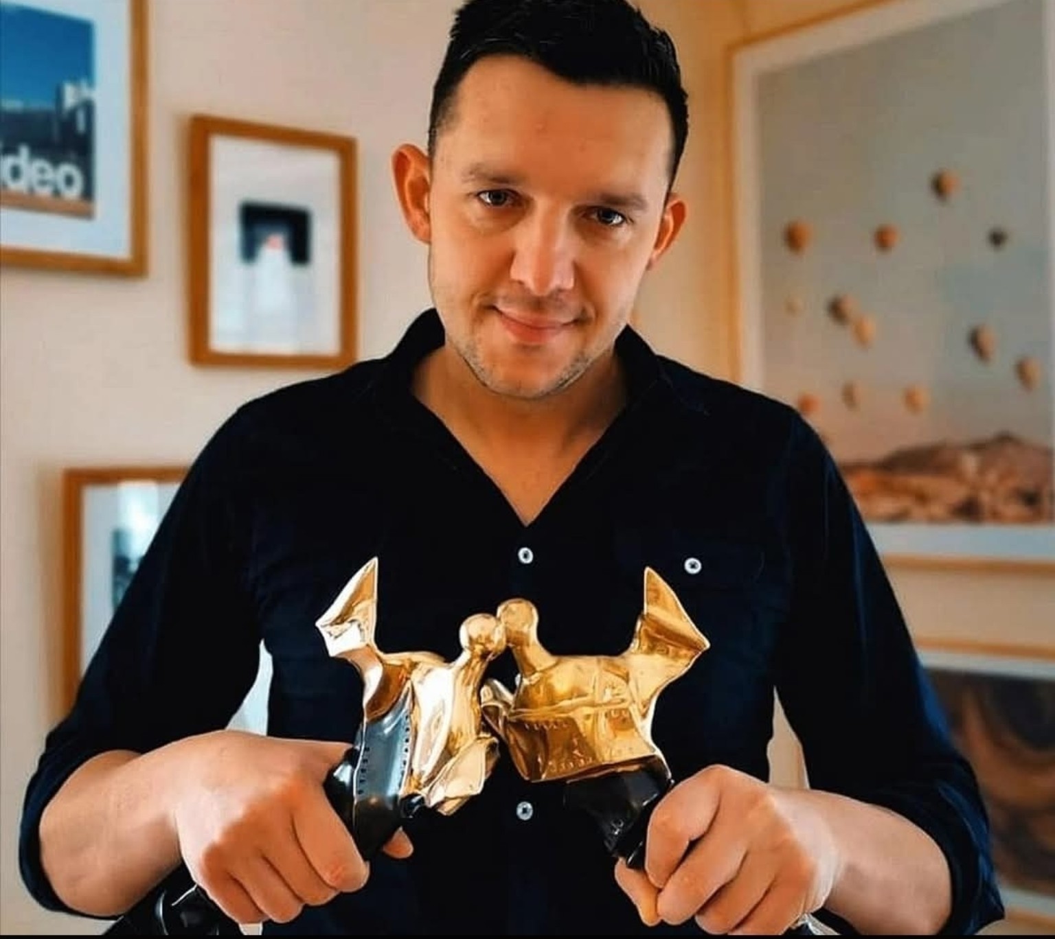 Adam Hartwiński holding two film award statuettes